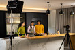 © Wavebreak Media - Diverse female team cooking and filming at kitchen island wearing apron, frying pan, camera