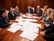 © backup_studio - Business meeting involves diverse professionals collaborating around wooden table covered with documents. Team engages in discussion with confident expressions and formal attire