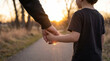 © David Zarzosa - Adult holding young child's hand while walking together along quiet rural path at warm sunset.