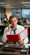 © Asmodar - Manager reviewing emergency response procedures while speaking on office telephone