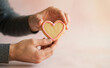 © SimpleDesignStudio - Adult man holding a heart shaped cookie with pink icing representing romantic love and valentines day