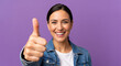 © Kamran - Cheerful woman in denim jacket giving thumbs up against purple background for success approval and casual lifestyle promotion