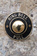 © Fotografia Juan Reig - Vintage brass and black door bell plate with ornate round pull mounted on an old stone wall, reflecting passerby and streetclassic residential entrance detail conveying historic charm and welcome
