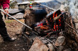 © Austockphoto - A person tending a fire pit using a long metal tool to adjust burning logs and embers