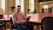 ©  VladaToday - Young adult university student reserving a quiet individual study desk while holding a tablet in a sunlit library, with private seating and an inviting academic environment