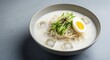 © Thilanphuong - bowl of kongguksu (noodles in cold soybean soup).  The thin white wheat noodles are submerged in a thick, creamy, frothy white soy milk broth with a couple of clear ice cubes floating. Garnish consist