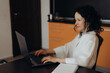 © YURIMA - Smiling woman works on laptop at kitchen table creating home office scene linked with freelance careers digital inclusion flexible work schedules online business confidence and modern work culture.