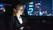 © SolaruS - A professional businesswoman sits in a car at night, focused on a tablet. The vibrant city lights create a hopeful, ambitious mood, perfect for corporate themes of success and latenight work.