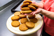 © Studio  GULL - female hands hold round golden-colored butter cookies with a wavy edge over a plate with pastries, product, classic shortbread, corn, yellow dough,