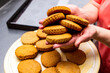 © Studio  GULL - female hands hold round golden-colored butter cookies with a wavy edge over a plate with pastries, product, classic shortbread, corn, yellow dough, biscuit, light background, sable, baker, bakery, but