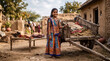 © Yash - Smiling young Indian girl in colorful traditional ethnic attire standing by a vintage wooden bullock cart in a rustic rural village setting with mud houses and warm sunlight.