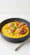 © farrezob - Delicious saffron risotto served with seared scallops and grilled shrimp in a dark bowl.