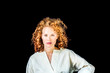 © Westend61 - Portrait of serious young woman with curly red hair in front of black background
