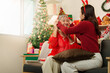 © Natee Meepian - Asian daughter placing festive Christmas headband on senior mother at home
