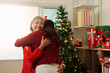 © Natee Meepian - Senior Asian mother embracing adult daughter by Christmas tree for seasonal family reunion