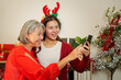 © Natee Meepian - Asian mother and daughter pointing at smartphone screen during Christmas holiday at home
