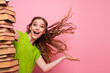 © deagreez - Young woman with green sweater laughs and hugs stack of book against pink background conveying study fun education energy and playful confidence