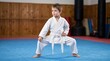 © Cahya - Young boy in white karate gi practicing low stance martial arts pose on dojo mat, depicting discipline, karate training, and kids self-defense practice