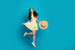 © deagreez - Joyful young woman in yellow dress jumping with straw hat against turquoise background, carefree summer fashion portrait showing movement, energy and happiness
