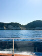 © Taya - View from a tour boat of white limestone cliffs and green pine hills across deep blue sea under a clear sky, boat wake and railing in the foreground, Greece