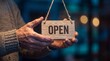 © artifexgenz - Weathered hands holding small rustic wooden sign with open text display for local shop business operations