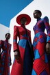 © Pete - Three black fashion models wear vibrant afrofuturism outfits with bold geometric patterns. Stylish women pose in red blue, purple haute couture clothes under blue sky. Modern african clothing trends