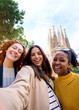 © CarlosBarquero - Vertical. Young only women friends taking selfie in front of Sagrada Familia, Barcelona. Beautiful mixed race girl on street of European city enjoying vacation happy and smiling. Funny tourism people