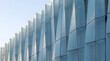 © Niki Visuals - Abstract architectural facade with repeating geometric triangular panels, light blue metallic building exterior with sharp angled vertical lines