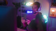© Krakenimages.com - Man wearing headset and microphone holds smartphone with both hands, gestures with left hand and smiles while seated in neon gaming studio; excitement.