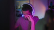 © Krakenimages.com - Man wearing white headset rubs eyes with hand while holding gamepad in gaming studio lit by purple led lights; fatigue.