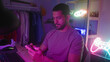 © Krakenimages.com - Man holding smartphone with both hands, thumbs tapping, neon gamepad sign and headset on desk visible in studio; focused relaxation.
