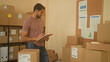 © Krakenimages.com - Man writing on clipboard while reaching with hand to pinboard amid stacked cardboard parcels and metal shelving in a storage building checking shipping labels and inventory; small business focus.
