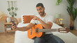 © Krakenimages.com - Man plays guitar and strums with right hand while holding a smartphone on a bedroom bed, smiling and gesturing toward the screen; relaxed practice.