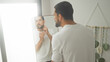 © Krakenimages.com - Young man touching face in mirror while applying skincare to his cheeks in a bright dressing area inside a building; confidence calm.