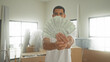 © Krakenimages.com - Man smiling, holding a fanned stack of dollars with right hand while standing among moving cardboard boxes in a building; celebration success joy.
