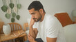 © Krakenimages.com - Young hispanic man with hand on chin sitting on bed beside notebook and lamp in a building; quiet contemplation.