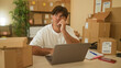 © Krakenimages.com - Man touches face while checking laptop and packages in a small business building; entrepreneurial planning contemplation.