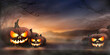 © Duncan Andison - A spooky sunset with the haunted evil glowing eyes of Jack O' Lanterns on the left and right of a wooden bench with copy space centre on a scary halloween night