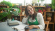 © Krakenimages.com - Woman florist in green apron writes on clipboard with pen at table surrounded by plants in studio; contentment planning.