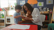 © Krakenimages.com - Woman seated holds a plush monkey while a little boy gently touches its paw and hands it a small toy over a low table in a building; bonding warmth nurturing.