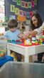 © Krakenimages.com - Woman and little boy play with colorful building blocks at a table inside a building, hands pointing and stacking bricks; playful learning.
