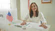 © Krakenimages.com - Woman sorting and stacking ballots with hands on table in building beside us flag and vote booth, arranging envelopes, pen, sticker roll and clipboard; civic pride.