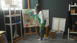 © Krakenimages.com - Woman painter wearing green apron and headphones holds paintbrush at easel while painting in studio; joyful creativity.