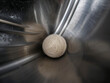 © Toufiqul - A small white ball of yarn resting inside the smooth metallic drum of a washing machine with curved steel walls and reflective silver surfaces