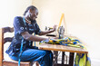 © Riccardo Niels Mayer - African seamstress uses a sewing machine while holding a phone to her shoulder, with measuring tape and colorful fabric, showing skilled work and female entrepreneurship