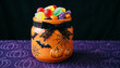 © ANDERLIO ART - Frasco Naranja de Halloween con Dulces y Lazo Negro sobre Mantel Morado con Estampado de Calabazas / Orange Halloween Candy Jar with Black Bow on Purple Pumpkin Pattern Tablecloth