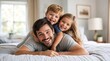© David - Happy father lying on bed with children playing and laughing together while enjoying quality family bonding time at home during weekend morning