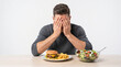© Madhushan - Young man resisting temptation to maintain healthy diet choices covering face from junk food burger isolated on clean white background