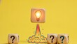© VectStocker - Lightbulb launching from a wooden block symbolizes a bright new idea, with question mark blocks nearby on a yellow background for brainstorm.