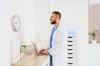© Pixel-Shot - Healthcare burnout and medical shift work, doctor using laptop in hospital office with clock showing time pressure and long hours in clinical practice